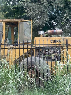 Yellow Clark earth-moving machine behind a wrought iron fence in tall grass outside Rogers, Arkansas